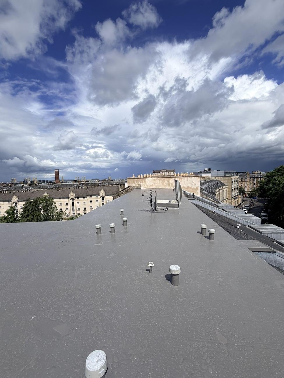 Completed liquid waterproofing membrane on an Edinburgh tenement flat roof, with the city skyline and chimney stacks behind
