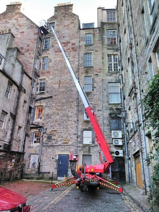 Tracked spider access platform reaching up a tenement building in a narrow Edinburgh close