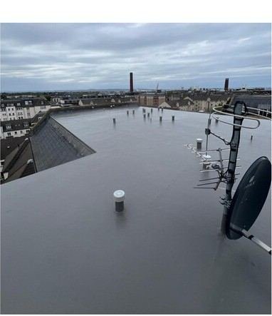 Finished grey liquid waterproofing membrane on a flat roof with chimney pots and Edinburgh rooftops behind