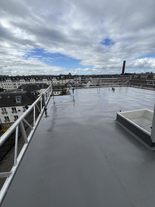 Completed flat roof membrane with rooflight and safety railing under a cloudy sky