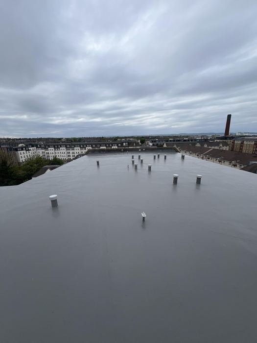 Completed flat roof membrane with rooftop vents under an Edinburgh sky, red chimney stack behind