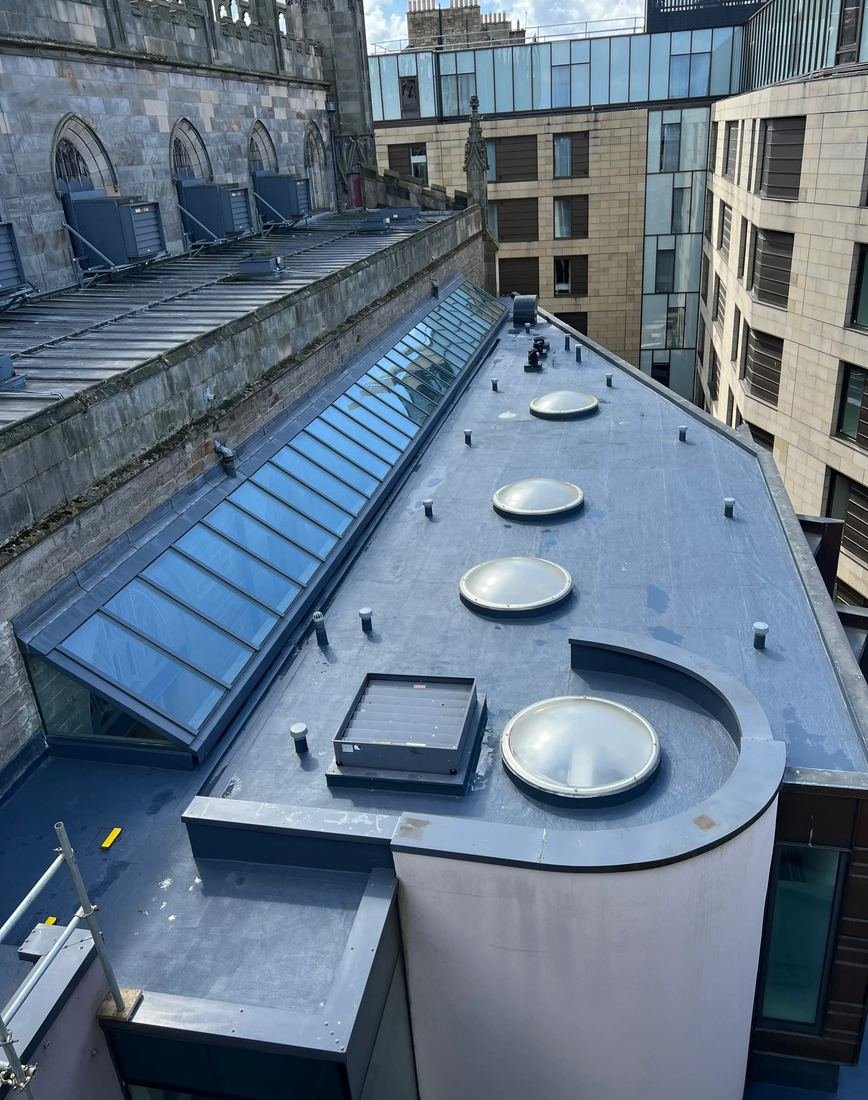 Rooflights and glass roof lantern on a completed flat roof, with sandstone church and modern glass building behind